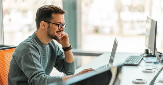 mann-im-pullover-mit-brille-laechelnd-vor-laptop