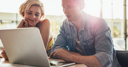mann-und-junge-frau-sitzen-am-tisch-vor-einem-laptop